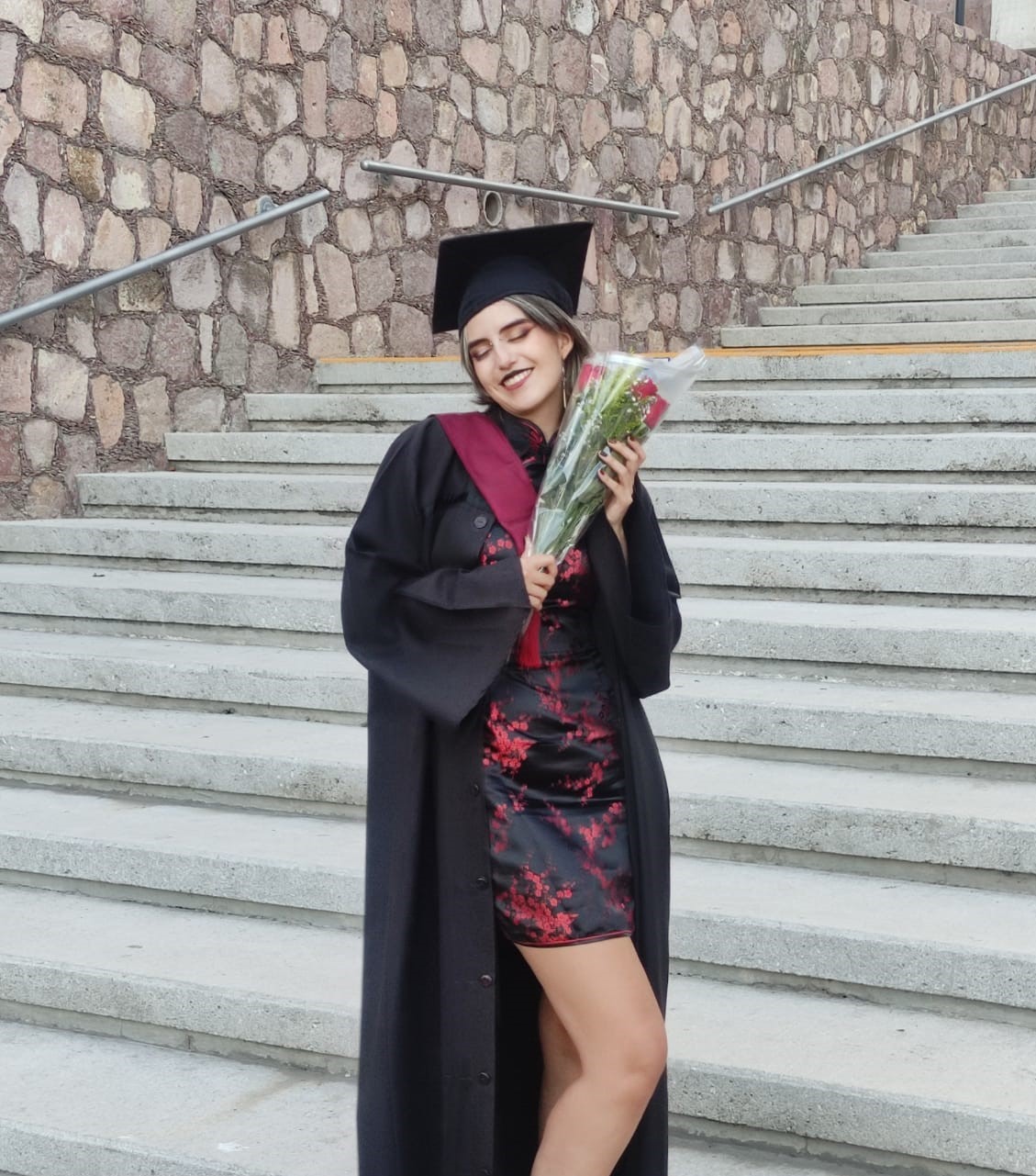 Picture of me holding flowers while wearing her graduation robe.